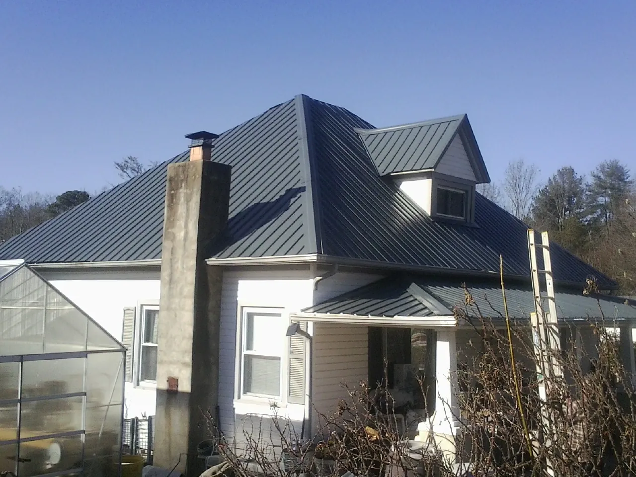 Dark blue standing seam metal roof on a white farmhouse with dormer — Slate & Tile Roof Repair by Roofing Brothers in Sanborn
