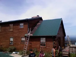 Green metal roof going on a two story log home with ladders set in Sanborn