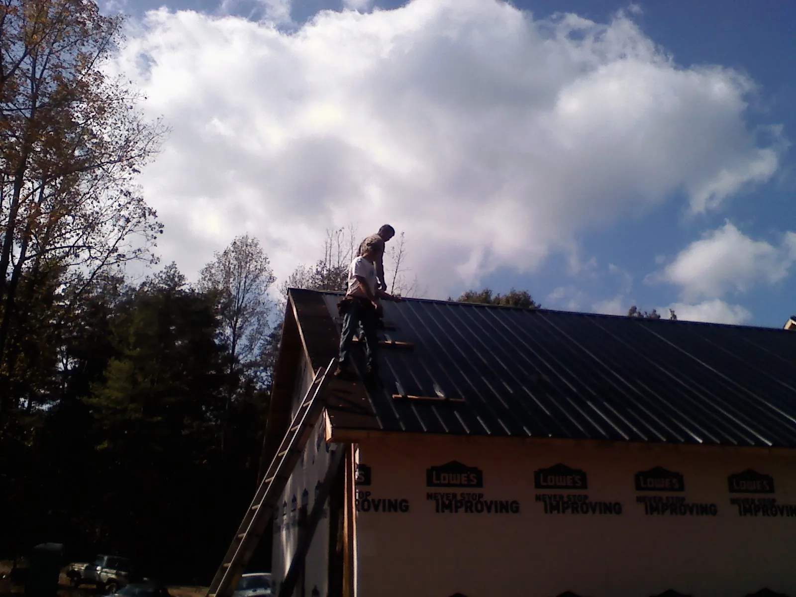 Roofer fastening dark metal panels high against a cloudy sky, from a Roof Inspection job in Sanborn