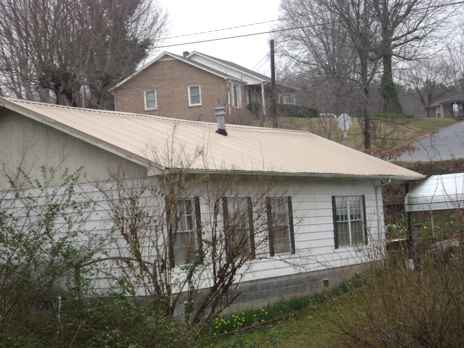 Tan metal roof on a white sided house set into a hillside — Commercial Roofing by Roofing Brothers in Sanborn